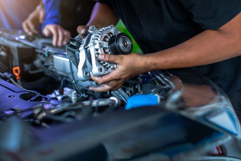 Mechanic replacing a car alternator in a vehicle engine bay, hands visible holding the part.