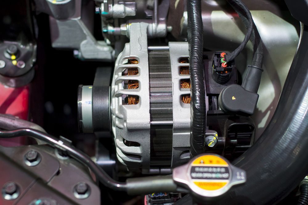 Close-up of a car engine, highlighting the alternator with copper coils and a black electrical connector. Cooling system is also visible.