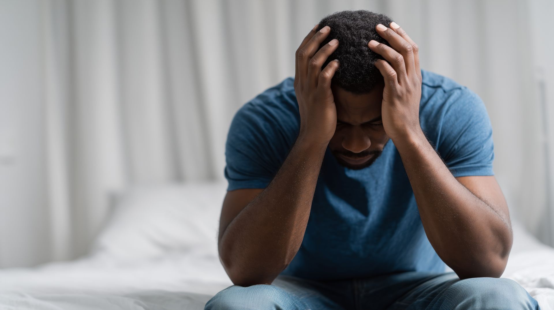 Therapist talking with a client on a couch in a bright living room office Man in a blue shirt sitting on a bed with his head in his hands, appearing stressed or distressed