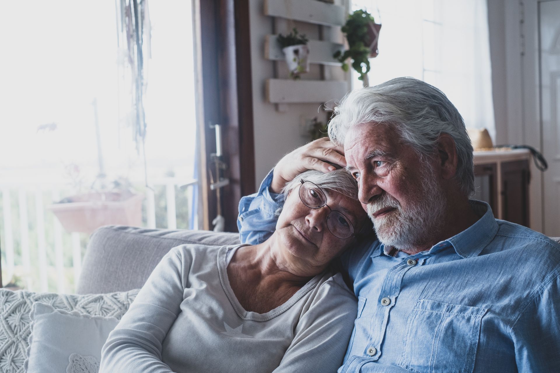 Two people talking on a couch, one gesturing with a raised finger in a bright living room Elderly couple sitting on a couch, with the woman resting her head on the man’s shoulder, both looking calm.