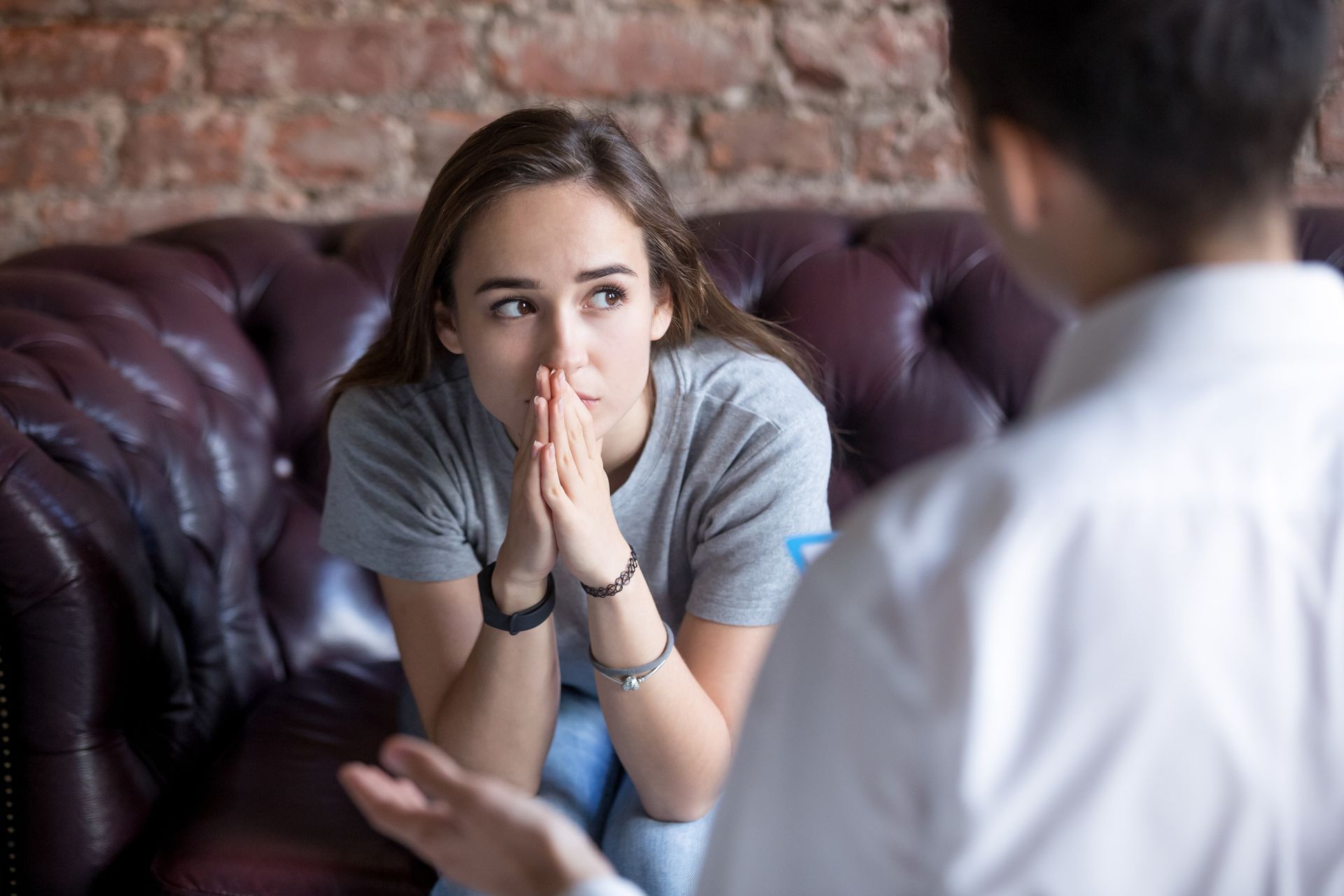 Two people in conversation on a couch, one listening intently with hands clasped.