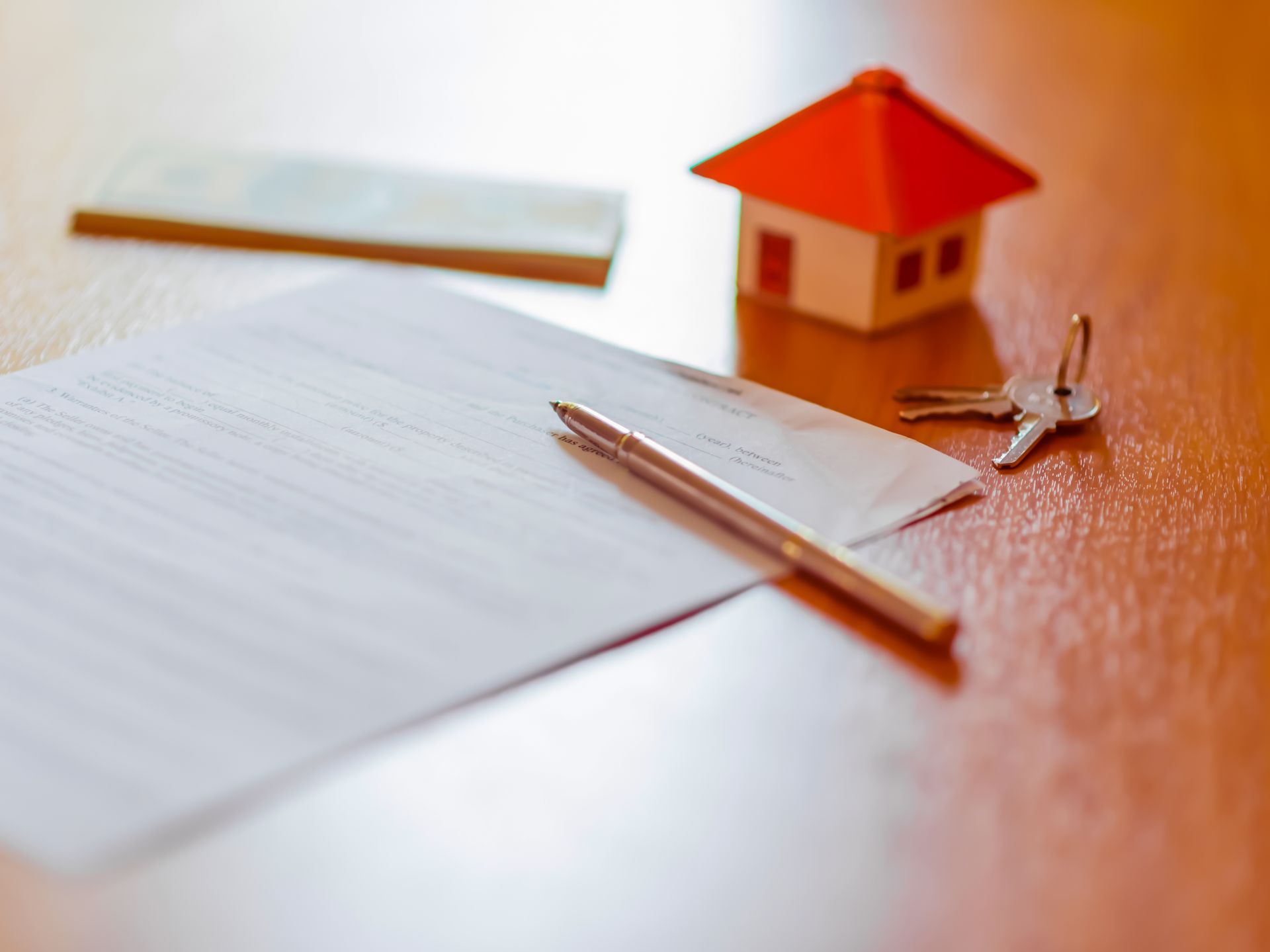 A pen is sitting on a piece of paper next to a model house and keys.