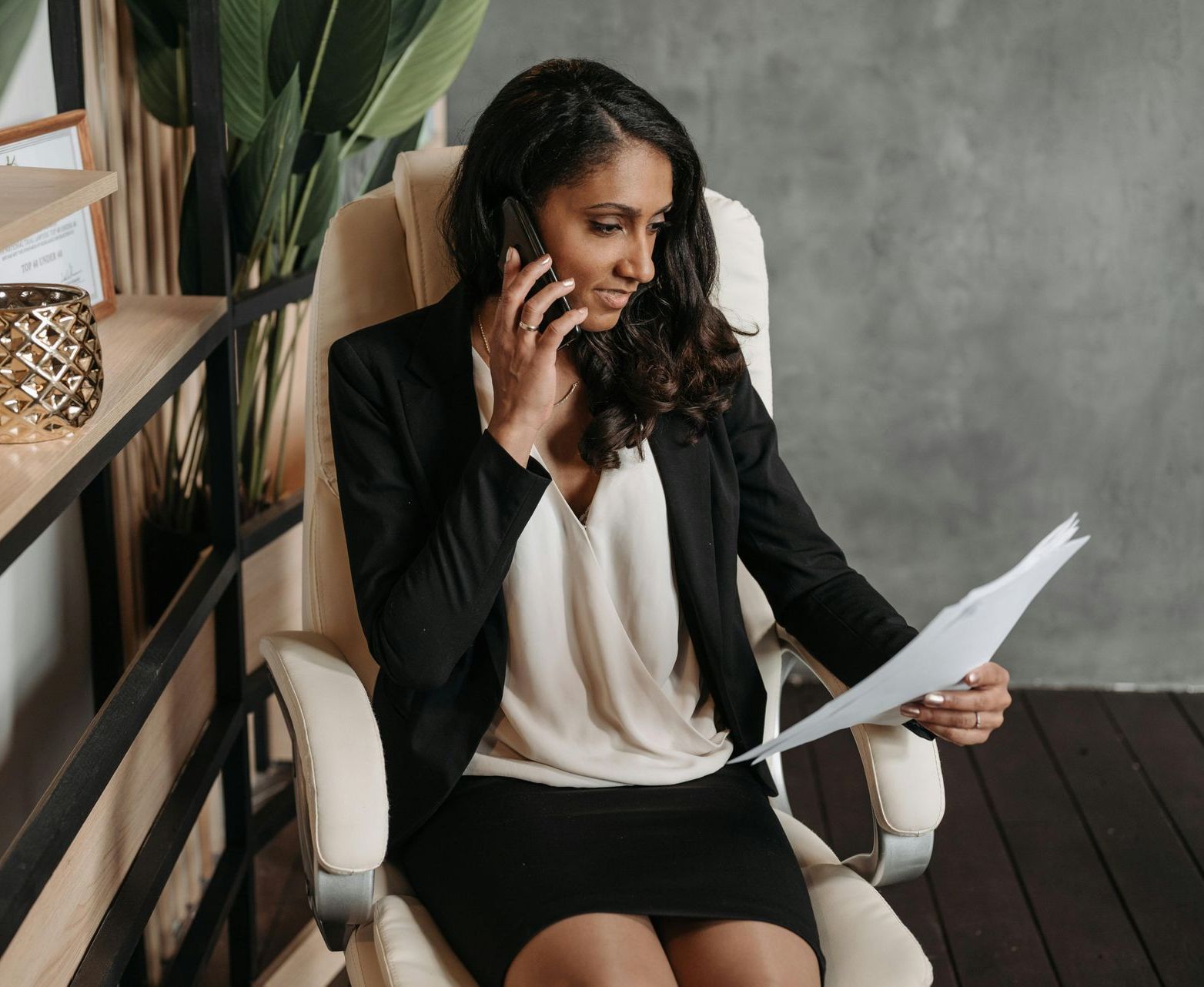 A woman is sitting in an office chair talking on a cell phone while holding a piece of paper.