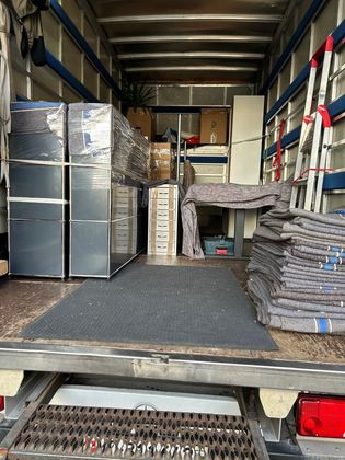 À l'intérieur d'un camion de déménagement rempli de meubles emballés, de cartons et de couvertures de déménagement, avec une rampe de chargement au premier plan.