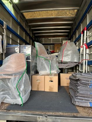 À l'intérieur d'un camion de déménagement rempli de cartons, de meubles emballés dans du papier bulle et d'une pile de couvertures de déménagement grises.