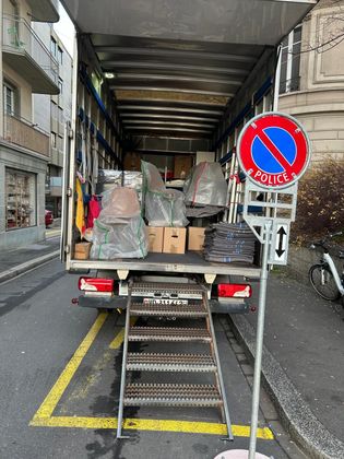 Un camion de déménagement est stationné dans une rue de la ville, avec un escalier portatif menant à la zone de chargement ouverte, à côté d'un panneau de police.