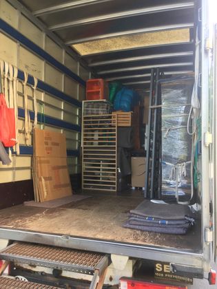 L'intérieur d'un camion de déménagement avec des cartons empilés, une étagère métallique, un sac bleu et des couvertures de déménagement au sol.