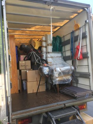 L'arrière d'un camion de déménagement ouvert, rempli de cartons, de meubles emballés et d'objets ménagers en vrac.