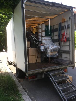 Un camion de déménagement stationné, porte arrière ouverte, laissant apparaître des cartons empilés et un fauteuil emballé dans du plastique à l'intérieur.