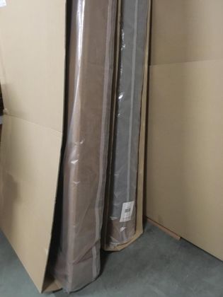 Deux boîtes longues et étroites, enveloppées dans du plastique transparent, se dressent debout sur un fond de carton brun uni.