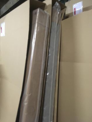 Deux objets longs et rectangulaires, emballés dans du plastique transparent, sont rangés debout à l'intérieur de conteneurs d'expédition en carton beige.