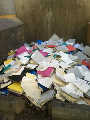 Un tas de dossiers colorés et de feuilles volantes jetées jonchent un coin en béton.