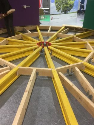Des ouvriers du bâtiment assemblent une structure circulaire en bois avec des poutres jaunes sur un plancher à l'intérieur d'un bâtiment.