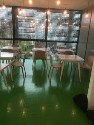 Des tables et des chaises de café vides, un sol d'un vert éclatant, devant une fenêtre munie d'un écran sombre à motifs.