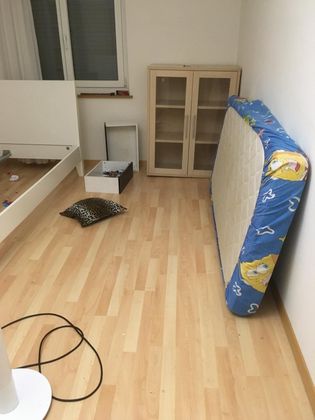 Une chambre meublée sommairement, avec un cadre de lit, une armoire, un matelas appuyé contre le mur et un oreiller posé au sol.