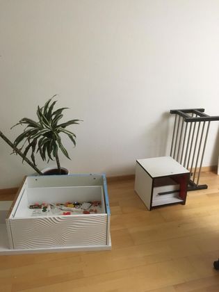 Une plante en pot, une caisse de rangement en bois blanc remplie de petits objets, une petite table d'appoint et un porte-serviettes posés au sol.
