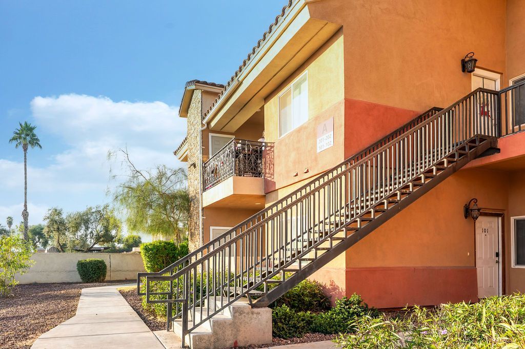 Exterior of an orange apartment building with a staircase. Palm tree visible in the background on a sunny day.