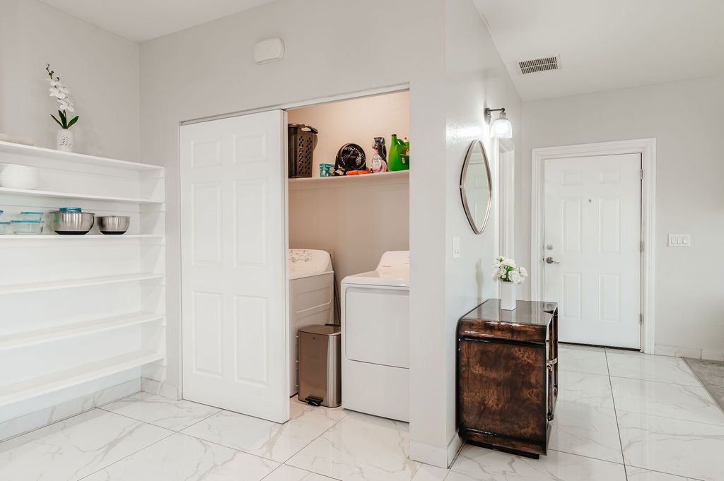 Laundry room with washer, dryer, shelves, and a storage cabinet. White walls, floor, and sliding doors.