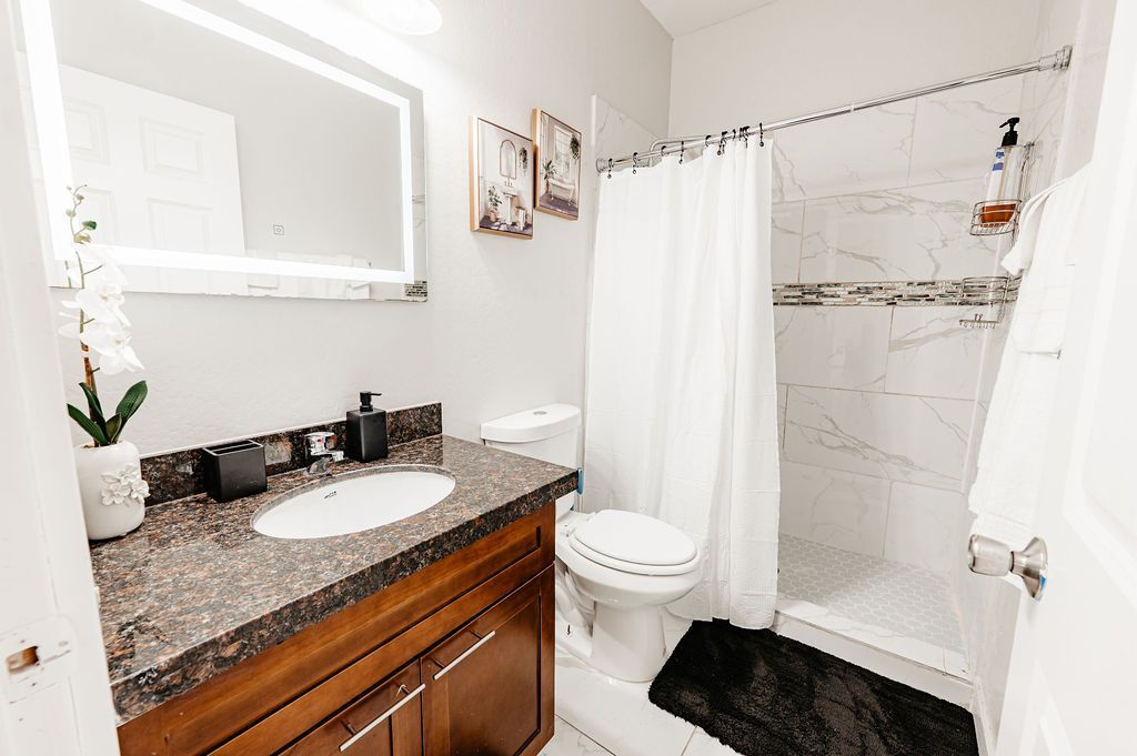 Bathroom with a vanity, toilet, and shower. The walls are white with a dark vanity countertop.