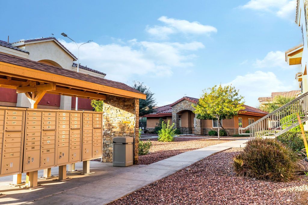 Apartment complex mailboxes line a walkway with buildings, sunny sky.