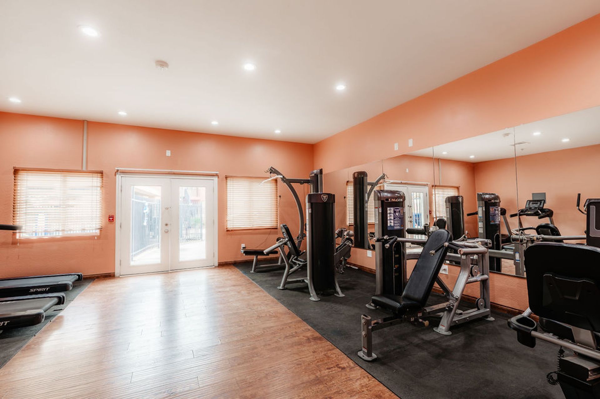 Gym with exercise equipment, including weight machines, punching bag, and treadmills. Peach walls and mirror.