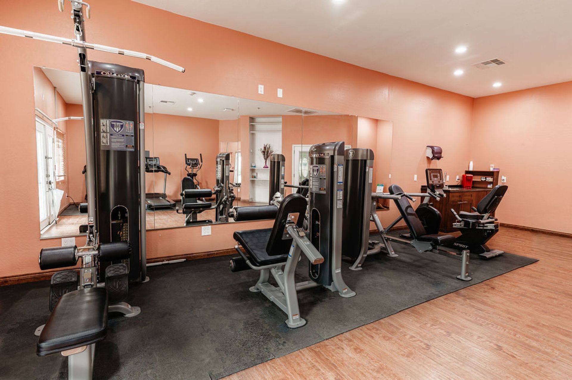 Gym with various exercise machines and a large mirror on an orange wall.