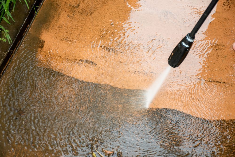 Worker Cleaning Driveway With Petrol High Pressure Splashing The Dirt And High Angle View — Local Gardener in Eaglehawk, VIC