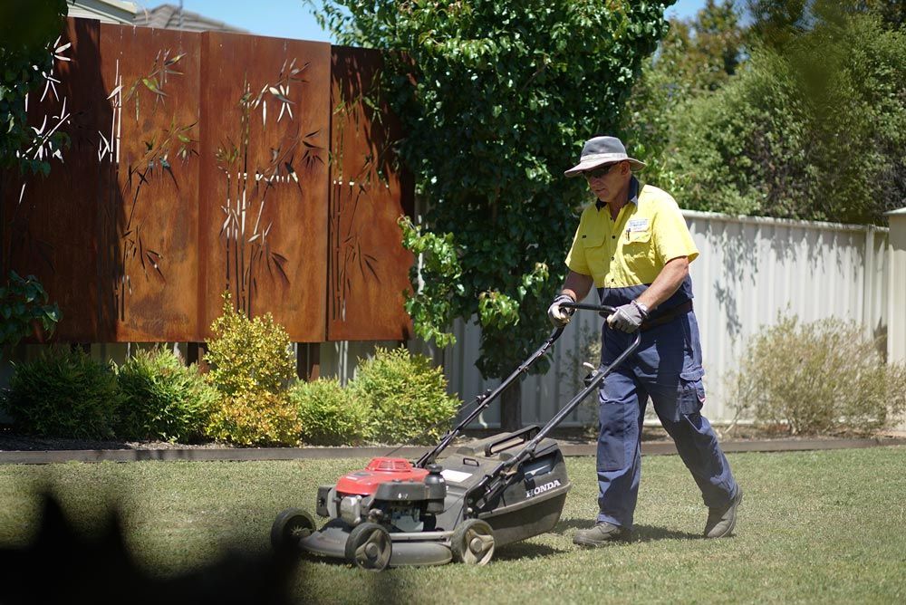 A Man Is Using A Lawn Mower To Cut The Grass — Local Gardener in Eaglehawk, VIC