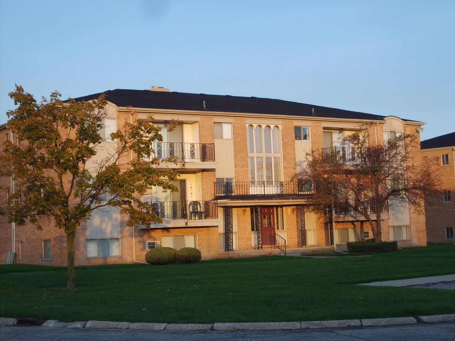A brick apartment building with balconies and trees in front of it