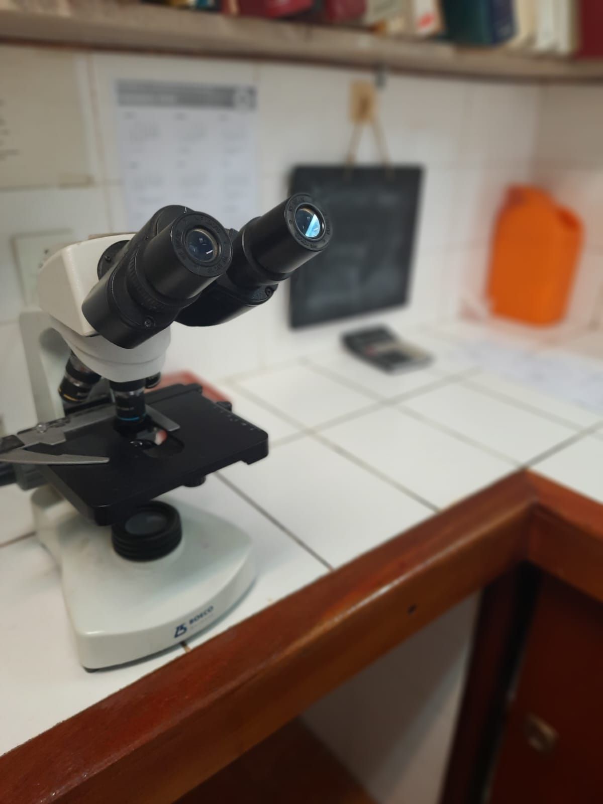 Un microscopio binocular blanco reposa sobre una encimera de azulejos blancos en un entorno de laboratorio