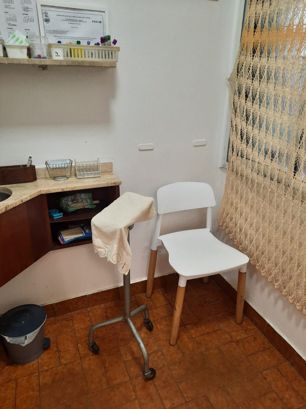 Una sala de exploración clínica con una silla blanca, un taburete médico con ruedas y funda de tela