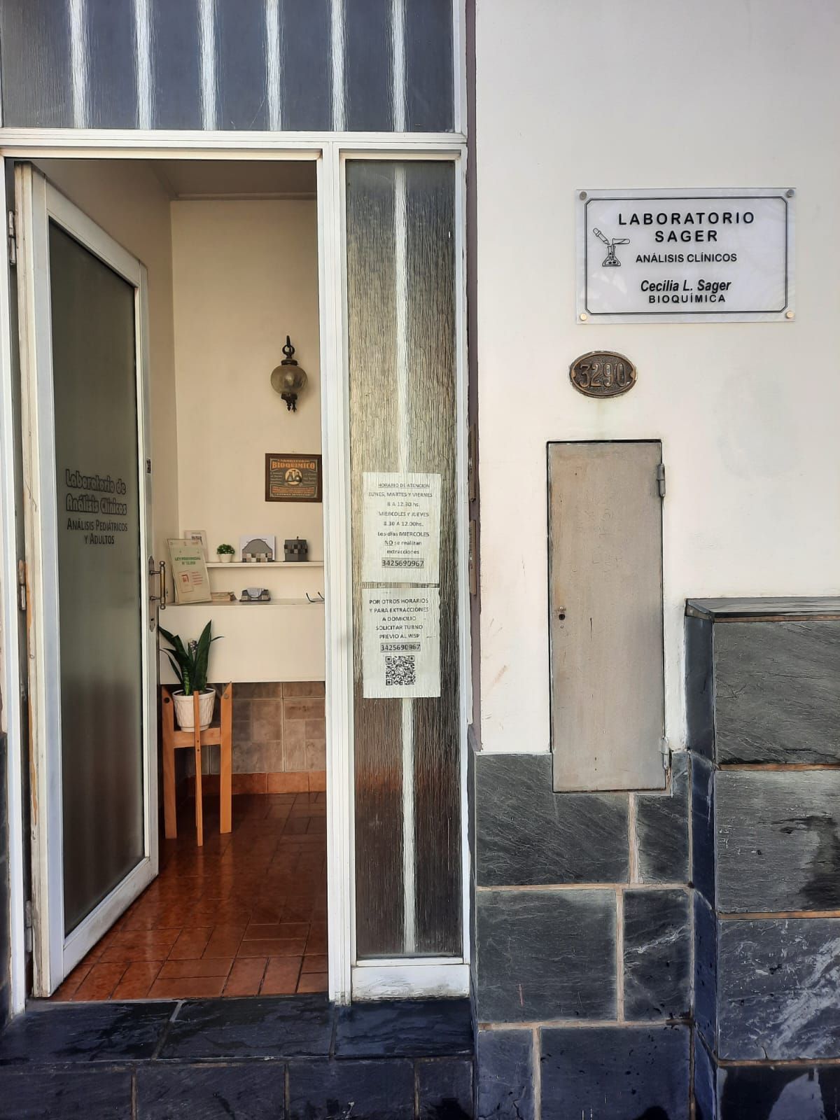Entrada abierta a un laboratorio dental con un letrero en la pared exterior blanca y una base de piedra