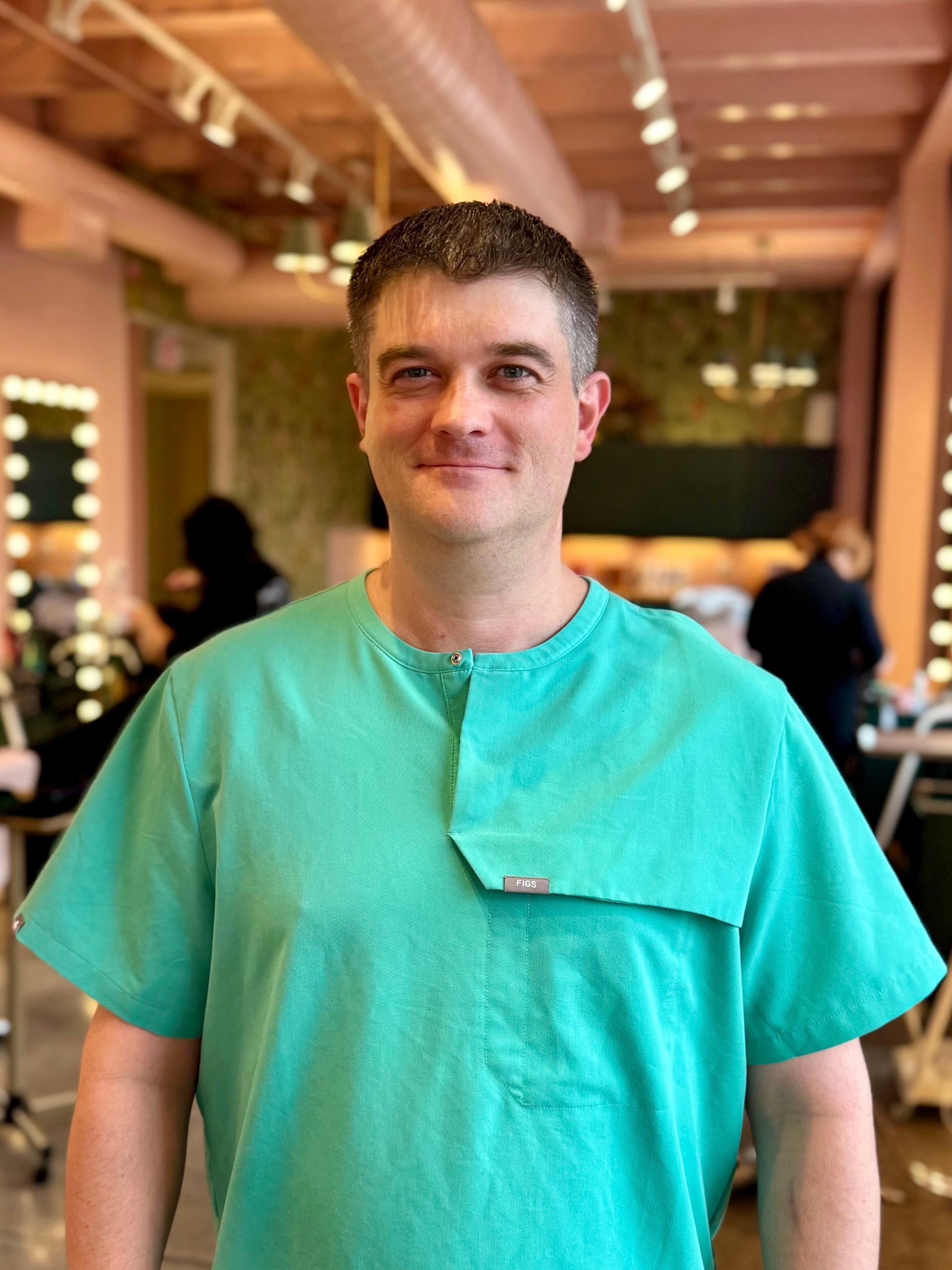 A man wearing a black polo shirt is standing in front of a white wall.