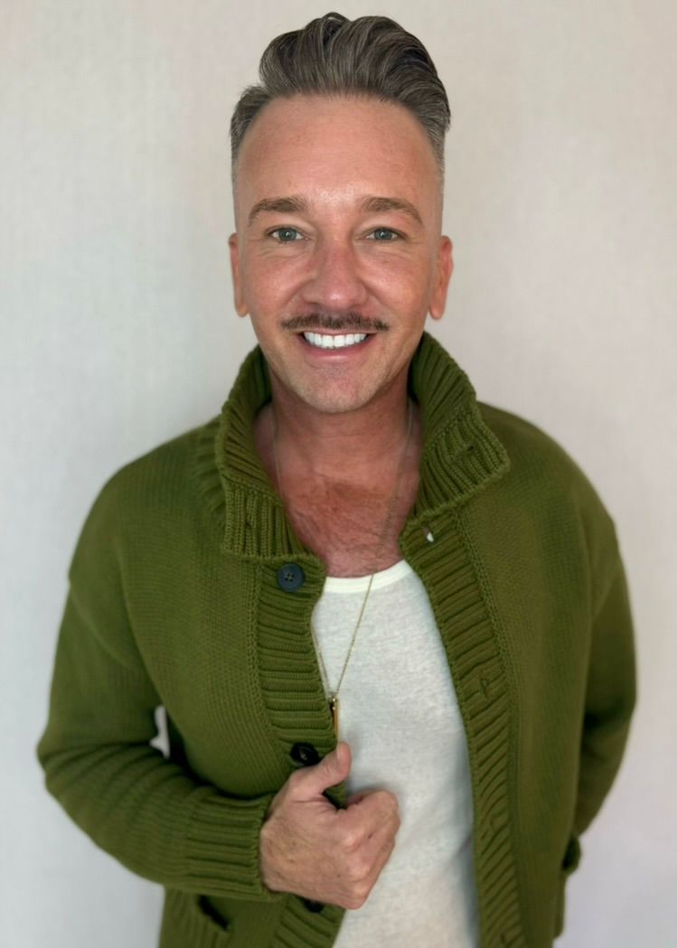 A man wearing a green sweater and a white shirt is smiling.