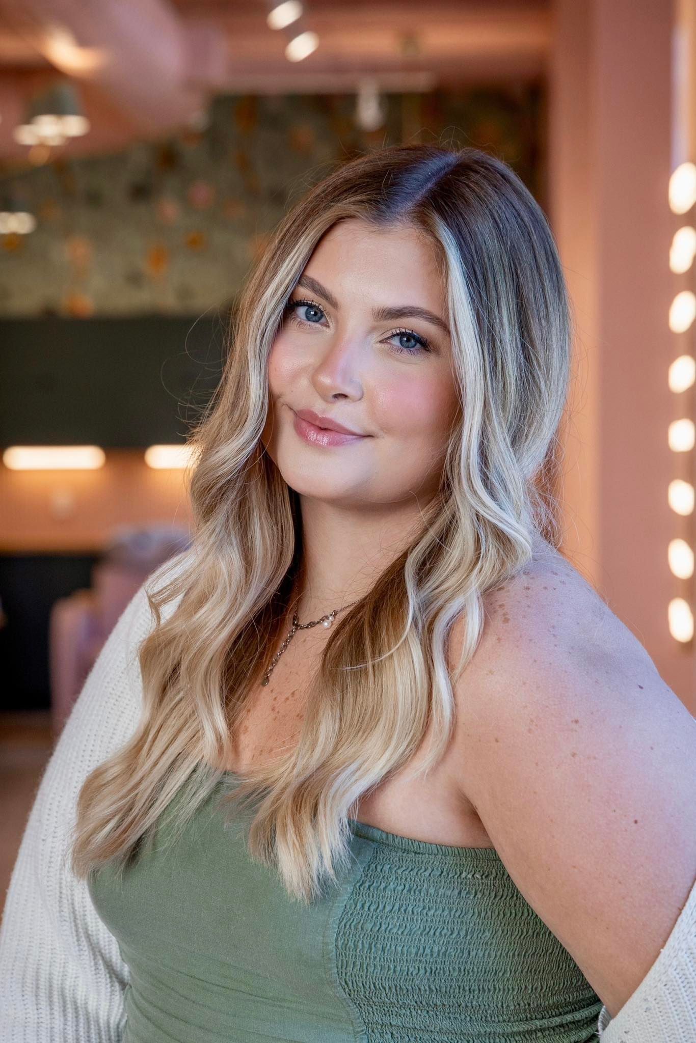 A woman in a pink dress is smiling and holding her hair.