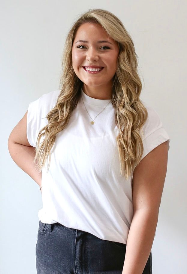 A woman wearing a white t-shirt and black jeans is smiling.