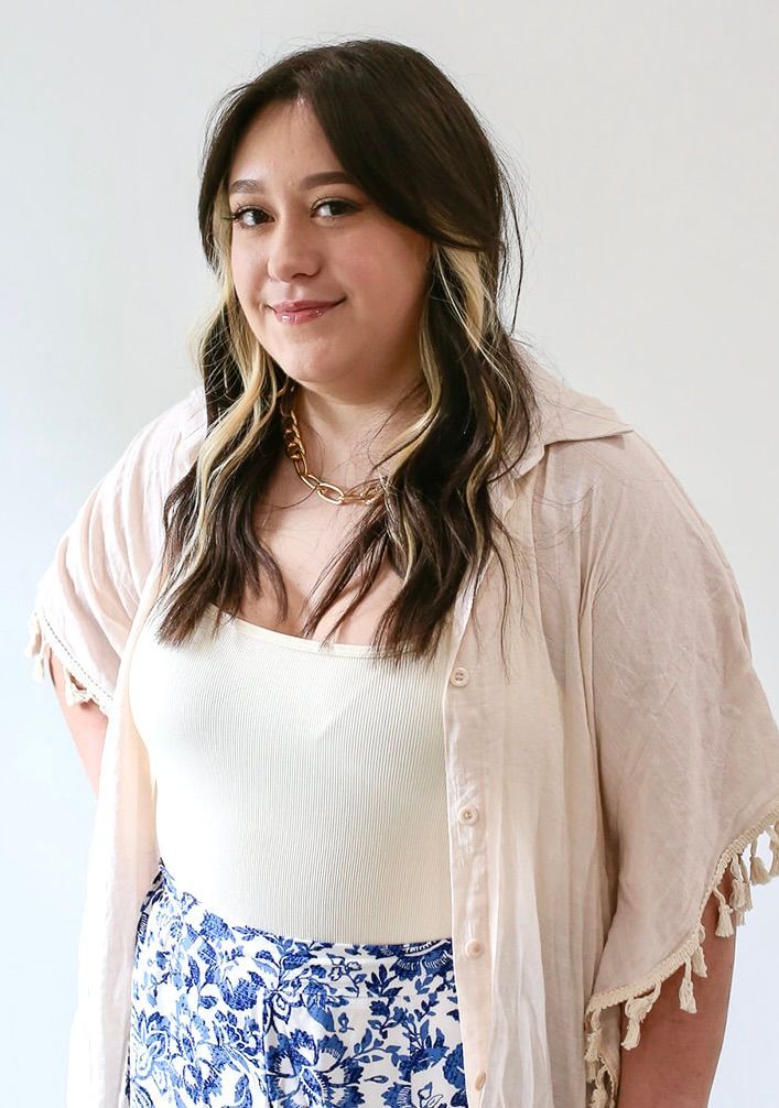 A woman wearing a white shirt and blue shorts is standing in front of a white wall.