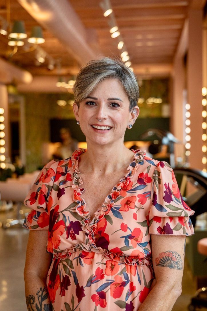 A woman with tattoos on her arm is smiling and standing with her arms crossed.