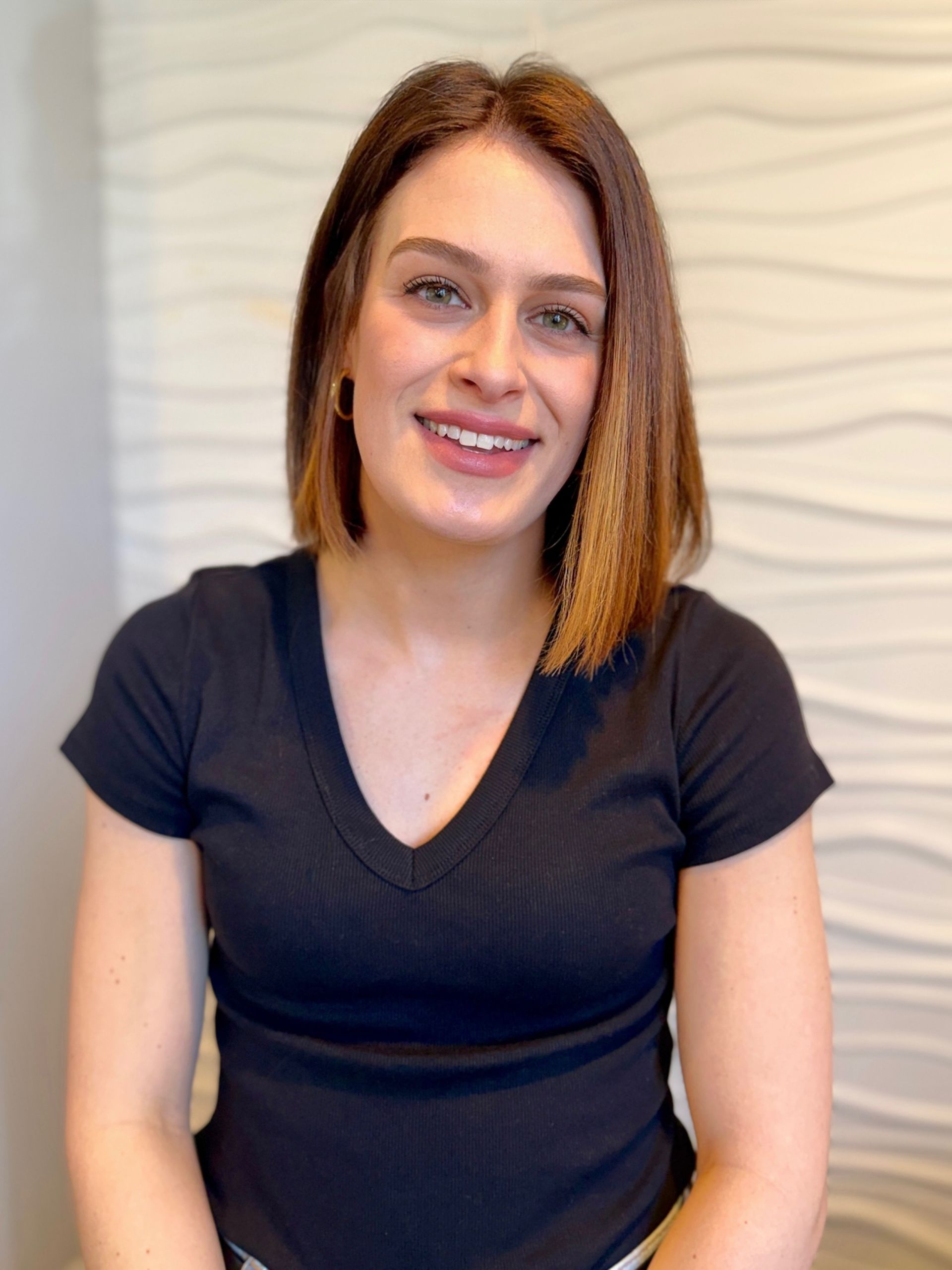 A woman wearing a striped shirt and jeans is standing in front of a white wall.