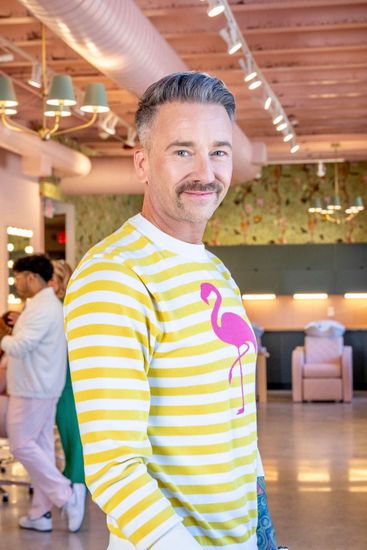 A man wearing a yellow and white stripe sweater with a flamingo on it and is smiling.