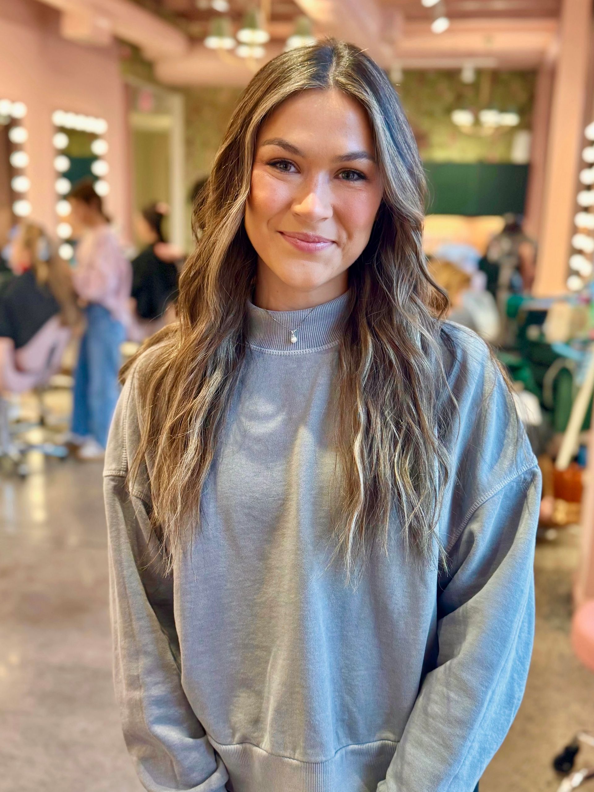 Woman smiles at the camera, wearing a pink sleeveless top; neutral background.