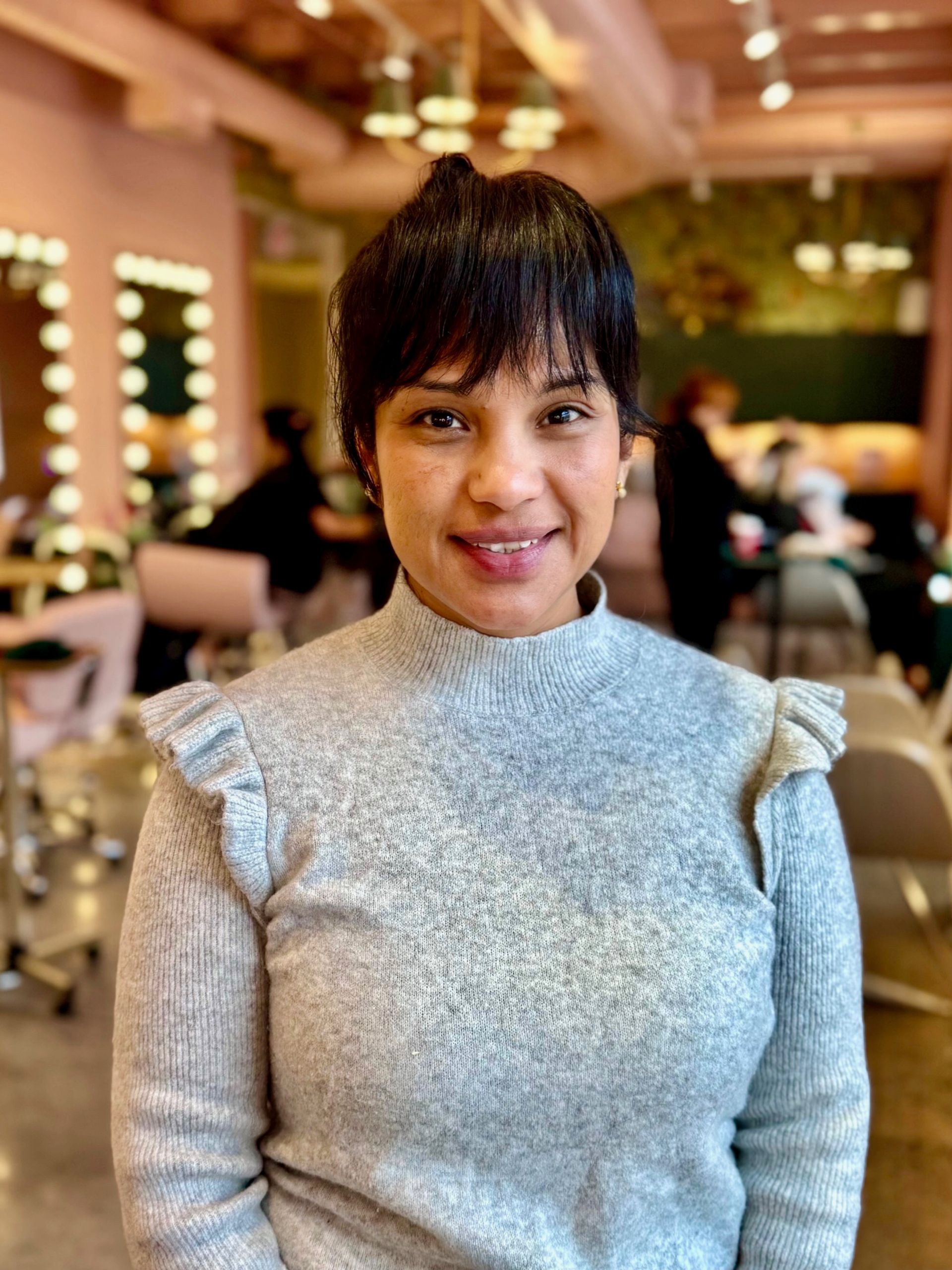 A woman is sitting in a chair holding her hair and smiling.