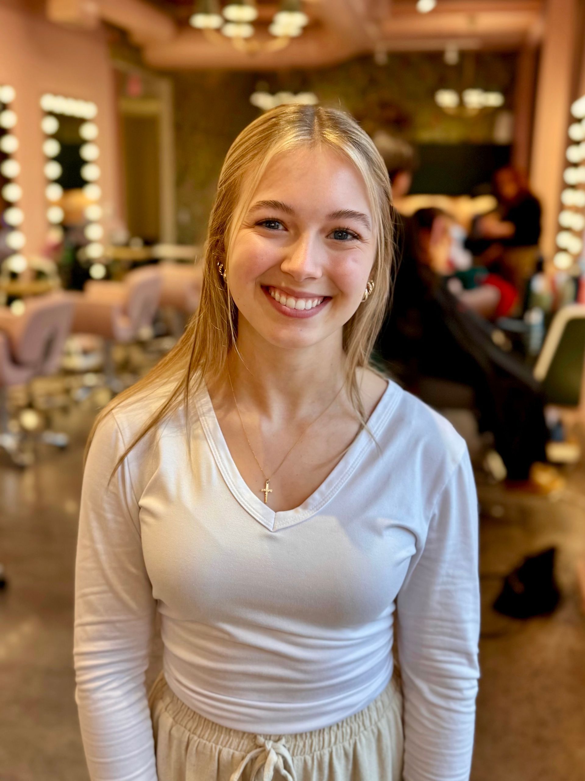 Blonde woman with a wide smile wearing a white tank top. Light gray background.