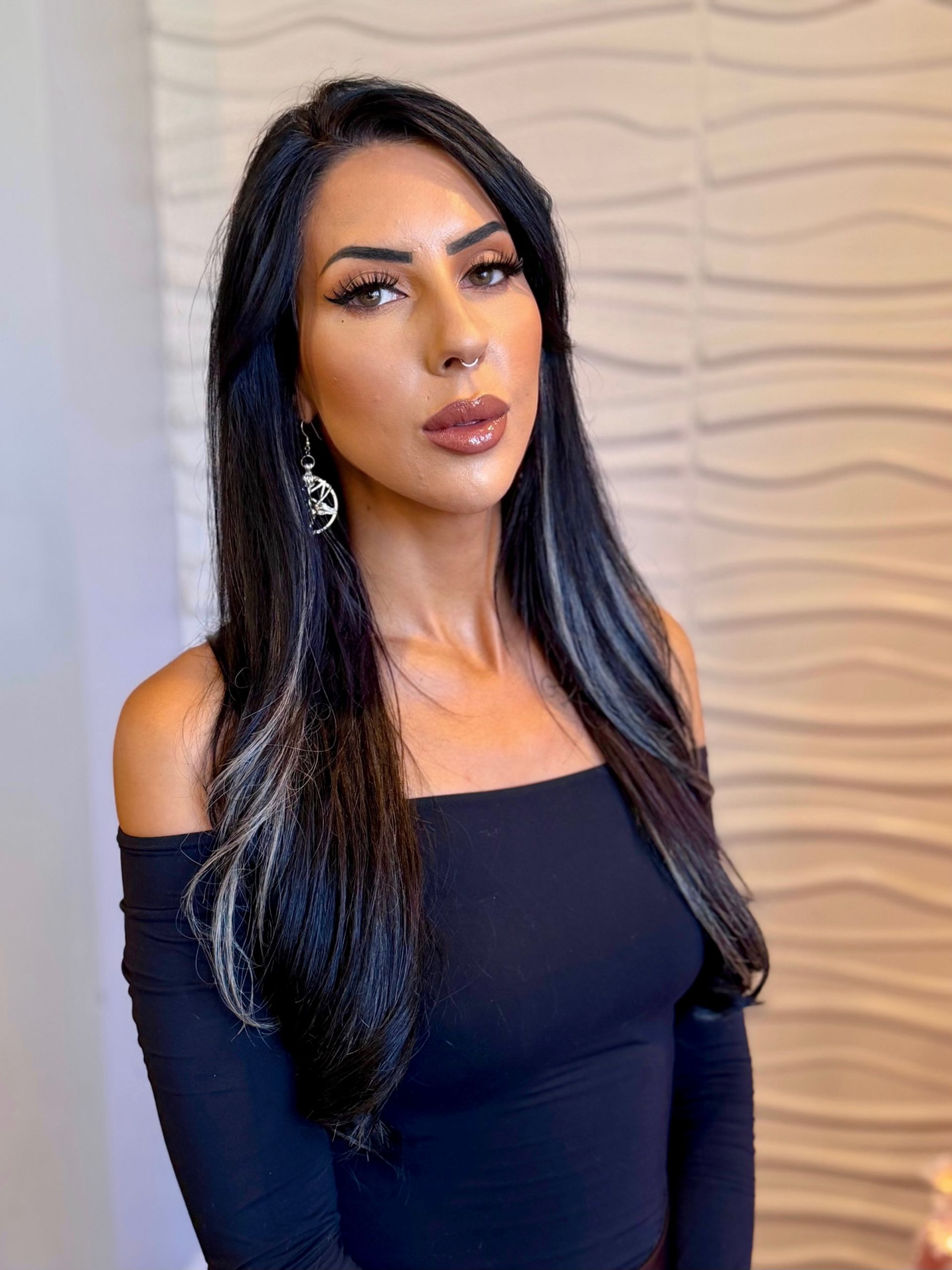 A woman with long black hair and a nose ring is wearing a black leather dress.