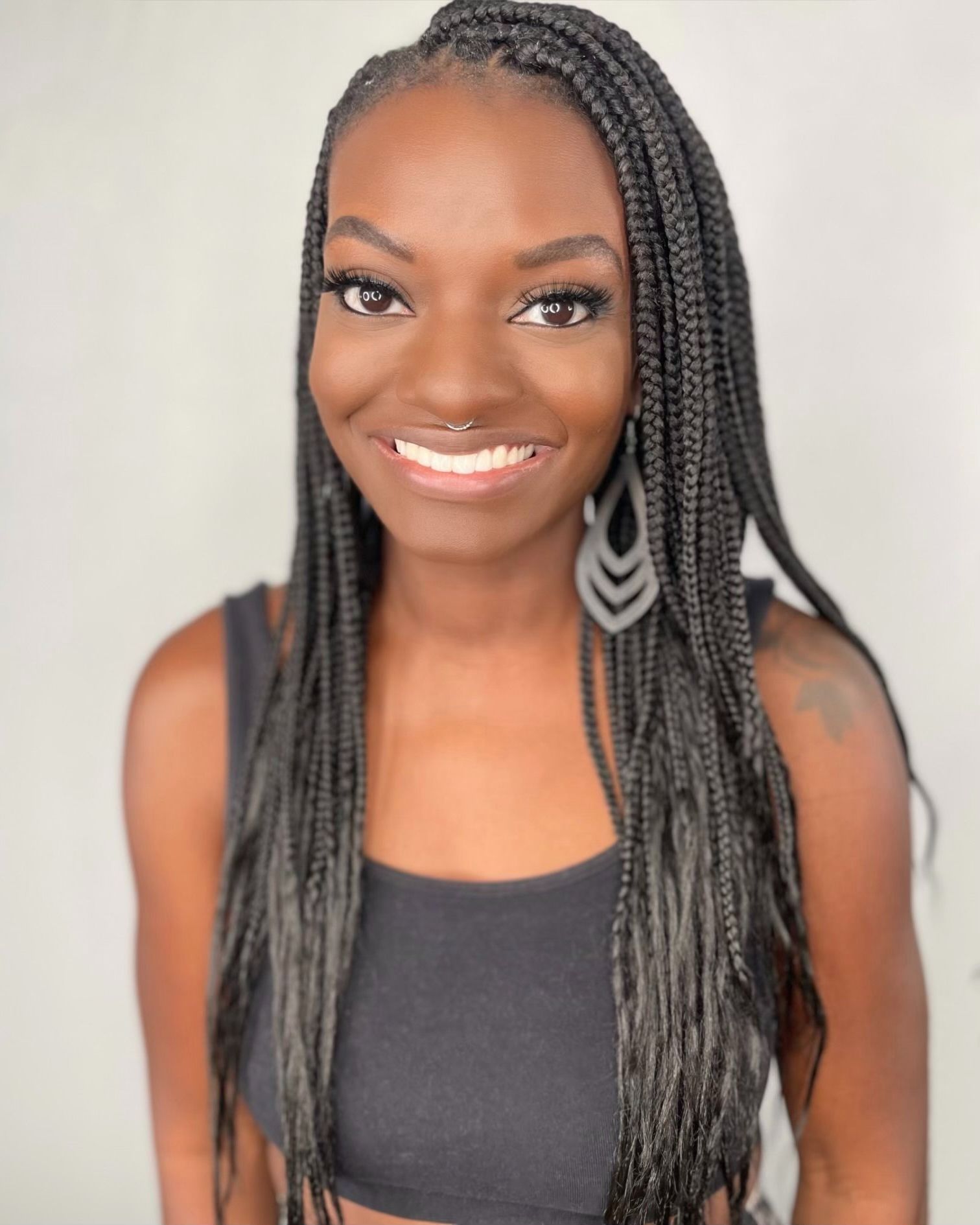 A woman with braids and earrings is smiling for the camera.