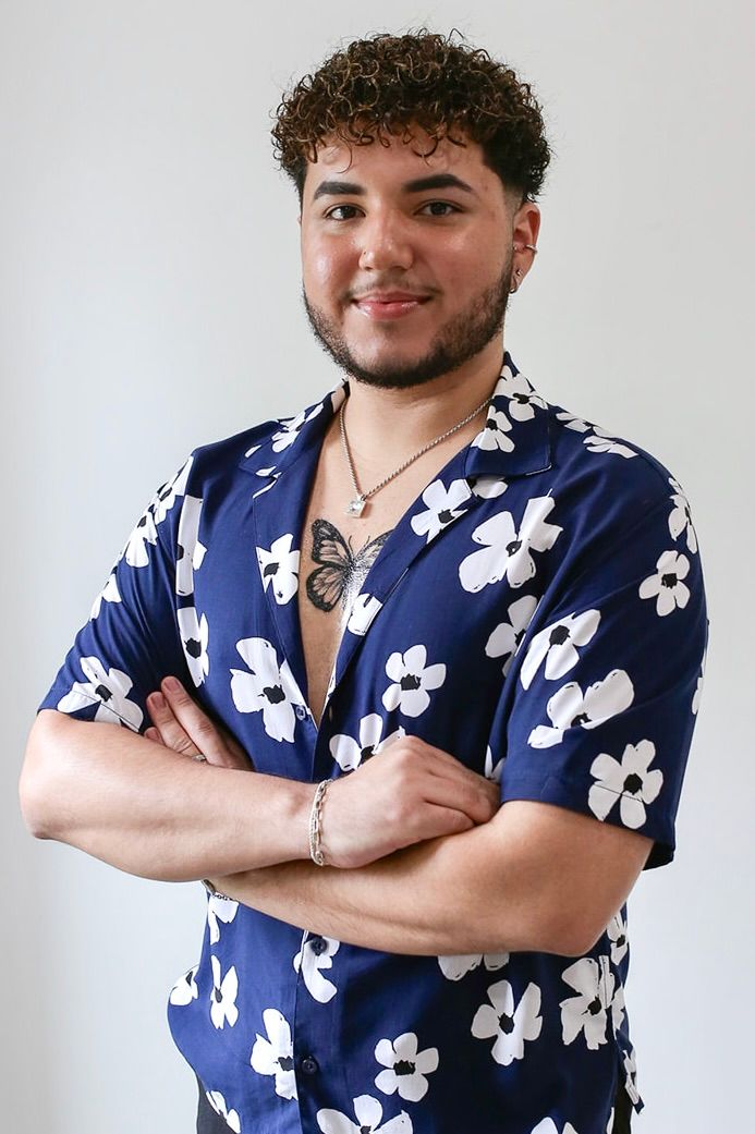 A man with curly hair is wearing a blue shirt with white flowers on it.