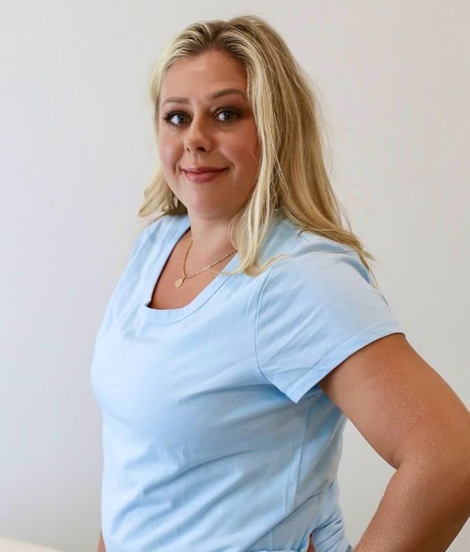 A woman in a blue shirt is standing with her hands on her hips