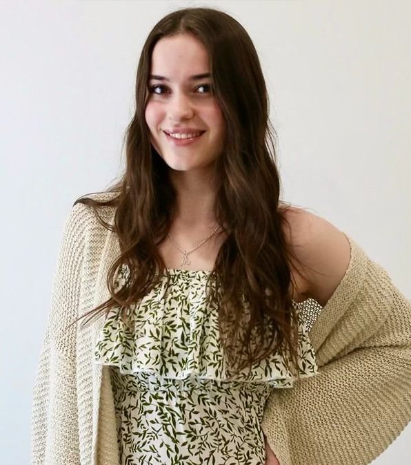 A woman wearing a sweater and a dress is smiling for the camera.