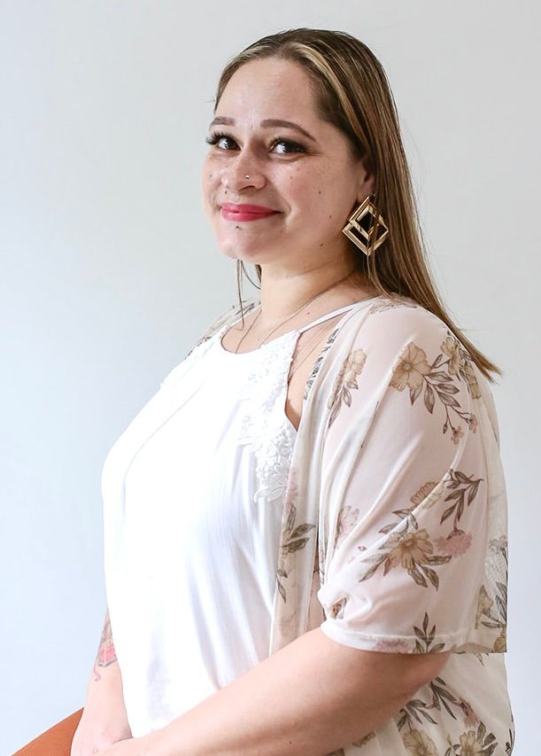 A woman wearing a white shirt and a floral kimono is standing in front of a white wall.