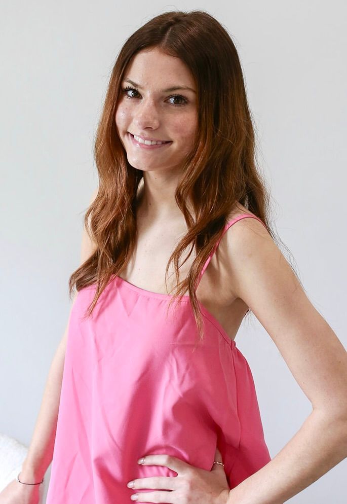 A woman in a pink tank top is standing with her hands on her hips.